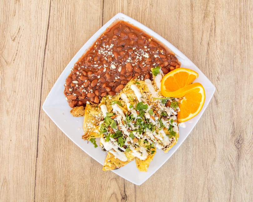 Chilaquiles with beans, cheese, cilantro, and sour cream, garnished with orange slices.
