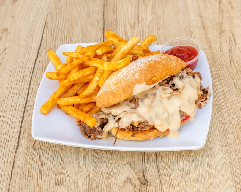 Cheesesteak sandwich with melted cheese, onions, and peppers, served with golden fries and ketchup.
