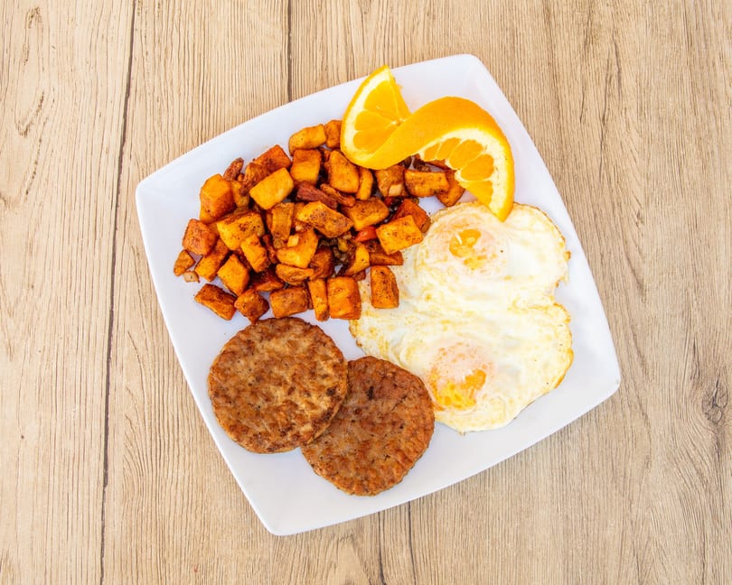 Breakfast plate with two fried eggs, two sausage patties, home fries, and orange slices.