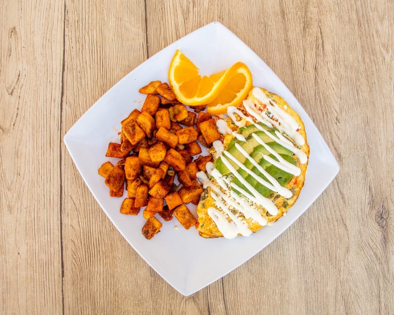 Omelet with avocado, sour cream, and cheese, served with seasoned potatoes and orange slices.