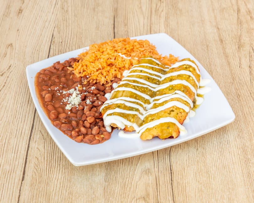 Two enchiladas with green sauce and sour cream, served with rice and beans on a white plate.