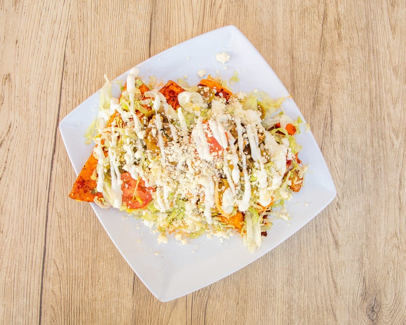 A plate of enchiladas covered in shredded lettuce, tomatoes, cheese, and white sauce.