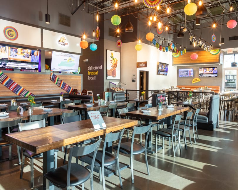 A vibrant, empty Mexican restaurant dining room with colorful decorations, wooden tables, and televisions.
