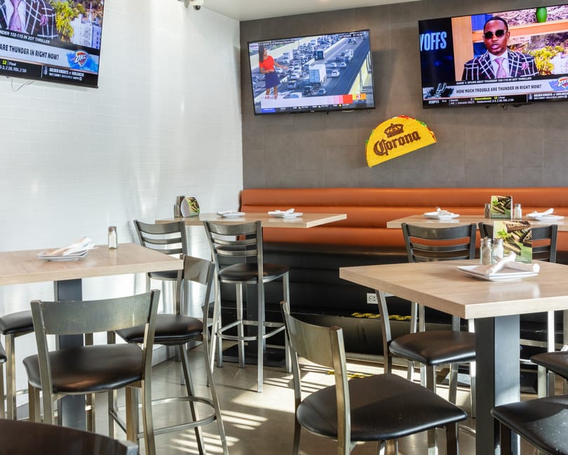 Restaurant interior with high-top tables, bar stools, an orange booth, and multiple TVs showing sports.