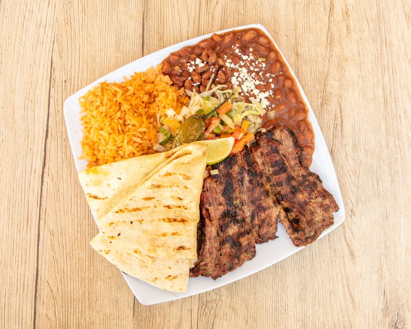 Grilled steak, rice, beans, salad, tortillas, and a lime wedge on a white plate.