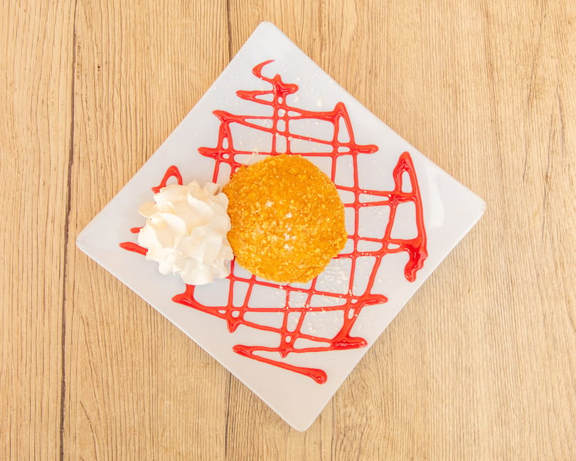 Fried ice cream dessert with whipped cream and strawberry syrup on a white square plate.