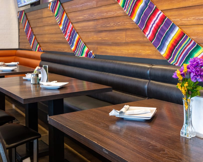 Restaurant interior with dark wooden tables, black and orange booths, and colorful striped fabric wall decor.