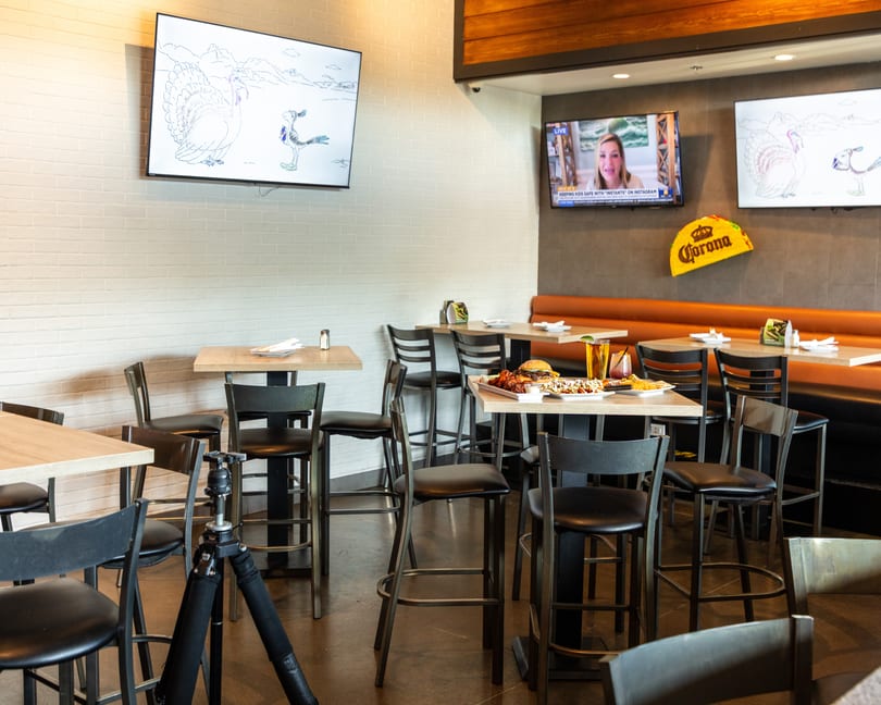 Restaurant interior with high-top tables, bar stools, a booth, and TVs showing news and cartoons.