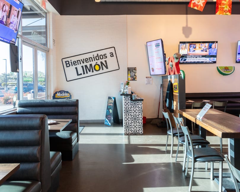 Interior of Limón restaurant with booths, tables, a welcome sign, and TVs on the walls.